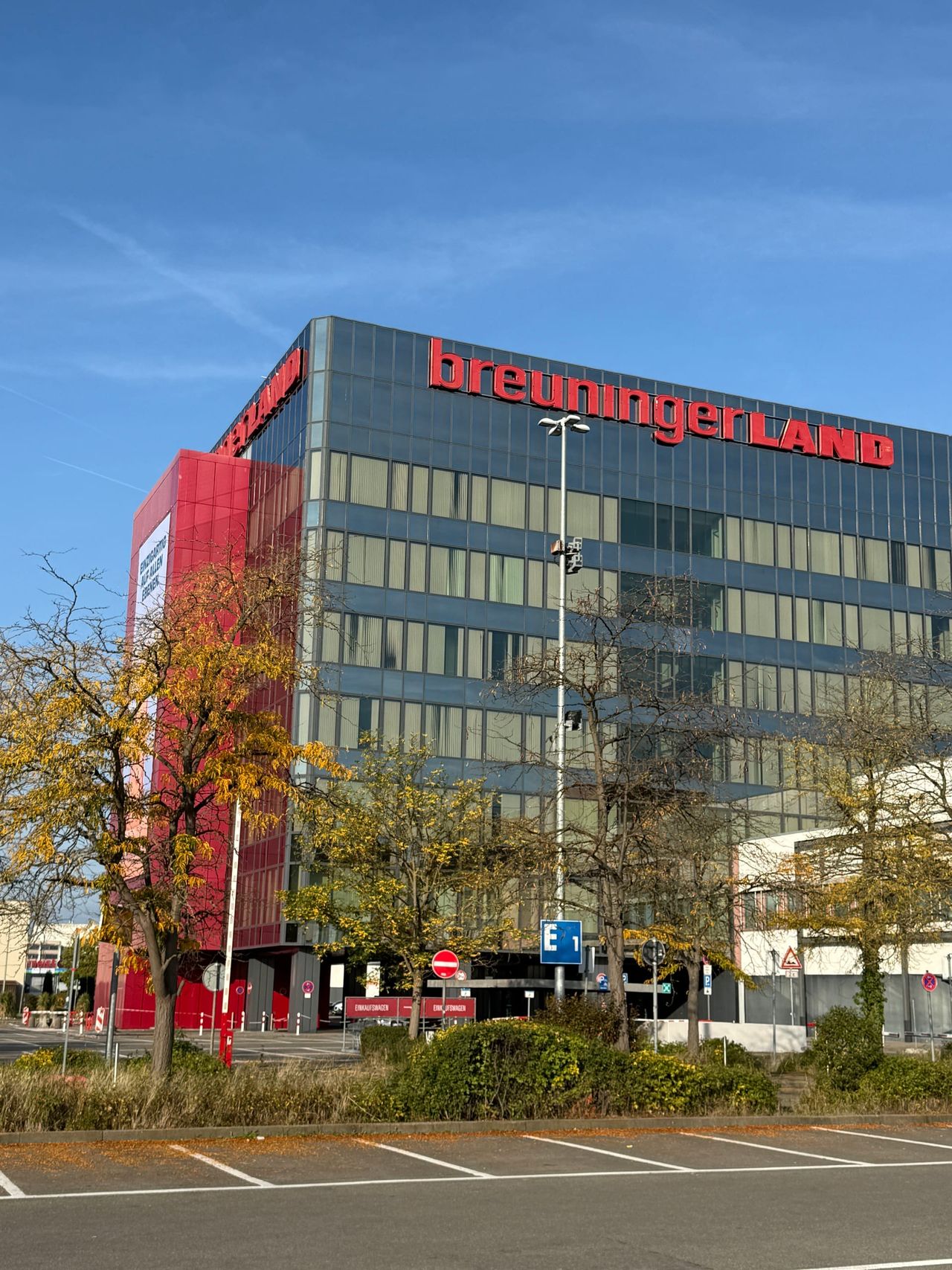 Hochformat der Glasfassade des Breuningerland Sindelfingen mit rotem Schriftzug und herbstlichen Bäumen