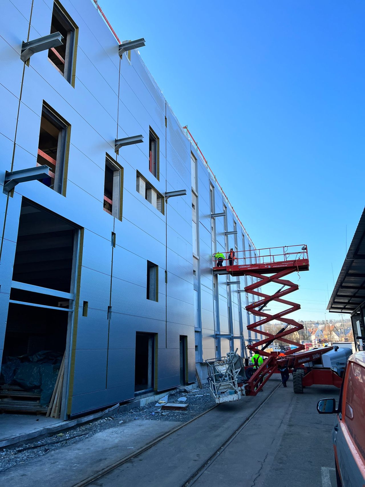 Hochformat der Lagerfassade mit Scherenhubbühne und Monteuren bei der Türmontage