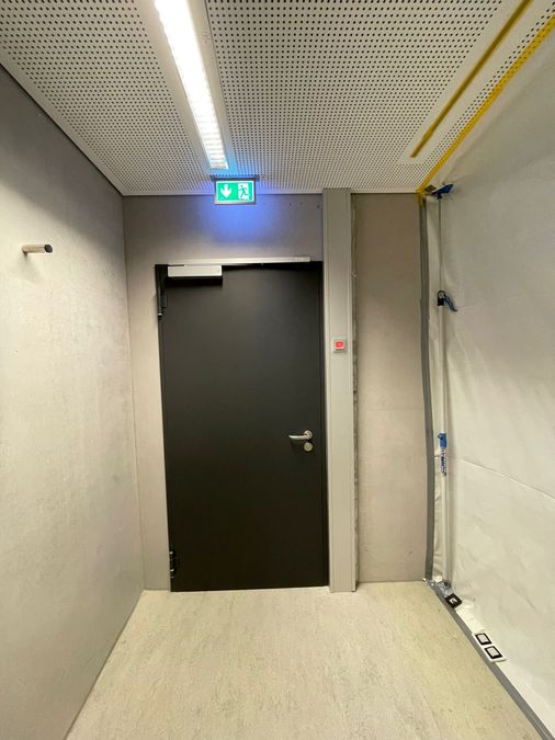 Brandschutztür im Korridor mit Feststellanlage, Rauchmelder und Fluchtwegkennzeichnung