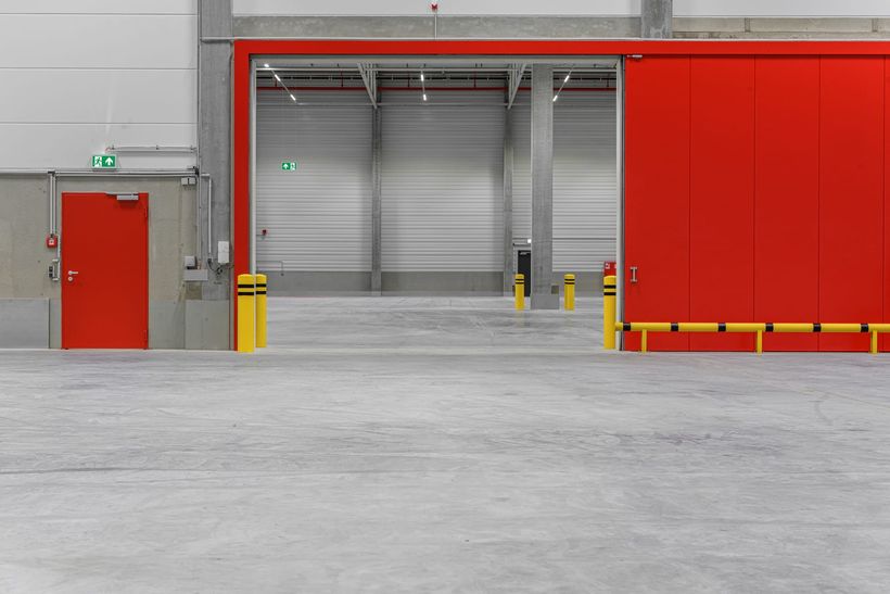 Rotes Brandschutz-Schiebetor in einer Logistikhalle, daneben eine rote Brandschutztür