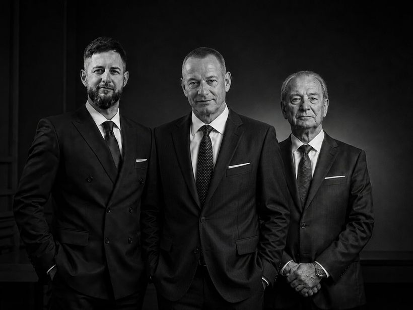 Chris, Bernd und Ludwig Ocker — drei Generationen der Unternehmerfamilie im Anzug vor dunklem Hintergrund